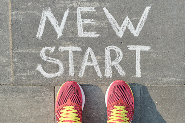 Word new start written on gray pavement with woman legs in sneakers, view from above